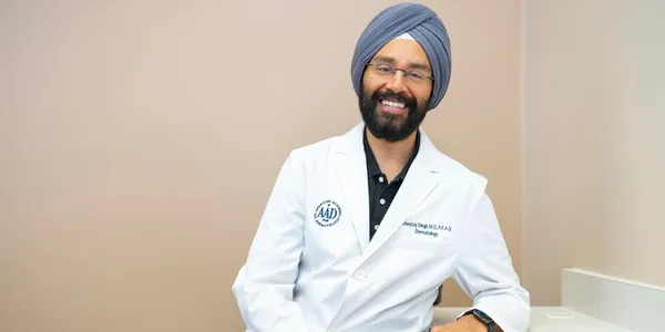 A man in white lab coat and turban smiling.